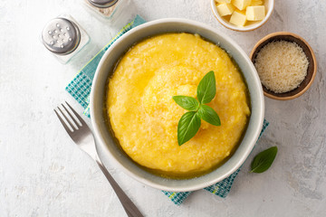 Polenta with butter and parmesan cheese in bowl on concrete background. Top view.