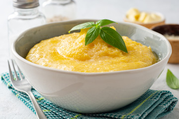 Polenta with butter and parmesan cheese in bowl on concrete background. Selective focus.