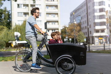 Father and children having a ride with cargo bike in a city