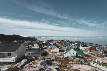 Aerial View of Arctic city of Ilulissat, Greenland. Colorful houses in the center of the town with icebergs in the background in summer on a sunny day with blue sky and clouds