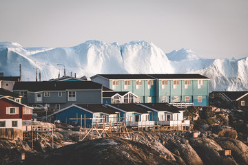 Aerial View of Arctic city of Ilulissat, Greenland during sunrise sunset with fog. Colorful houses in the center of the town with icebergs in the background in summer on a sunny day with orange pink - obrazy, fototapety, plakaty