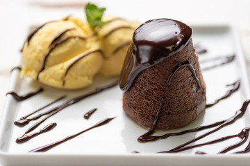 Petit gateau dessert; Petit gateau with vanilla ice cream and chocolate sauce in a white plate on white wooden background.