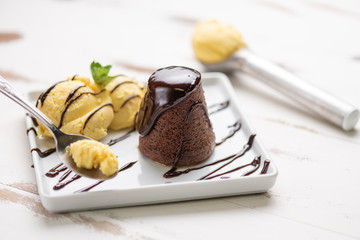 Petit gateau dessert; Petit gateau with vanilla ice cream and chocolate sauce in a white plate on white wooden background.