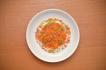 Sugar sprinkle dots, sprinkles in white saucer, on a wooden table, decoration for cake and bakery, top view
