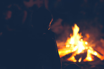 Boy with friends sitting near campfire and looking at the flame.