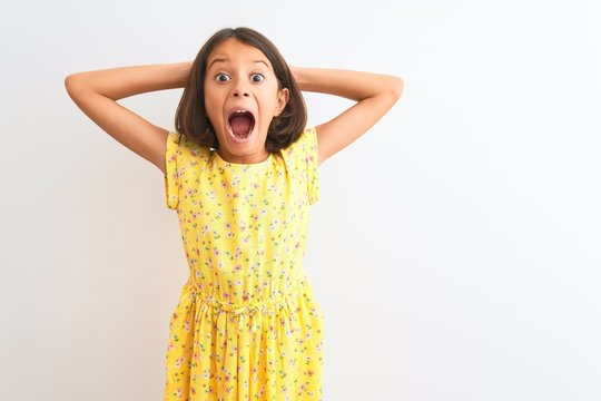 Young beautiful child girl wearing yellow floral dress standing over isolated white background Crazy and scared with hands on head, afraid and surprised of shock with open mouth