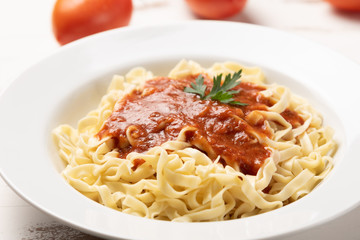 Fettuccine pasta with tomato sauce, parsley and basil in a white plate on a rustic wooden table background, soft light