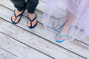 Feet of man and woman wearing flip-flops on wooden background