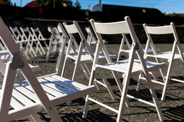 Symmetry of love: Rows of white folding chairs on lawn before a wedding ceremony in summer. White Folding Chairs at an Outdoor Wedding with flowers