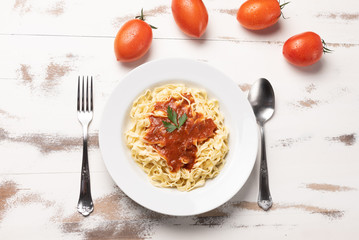 Fettuccine pasta with tomato sauce, parsley and basil in a white plate on a rustic wooden table background, soft light