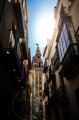 Fototapeta premium View of Giralda tower of Cathedral of Saint Mary of the See, Seville Cathedral, through a narrow street, Andalucia, Spain