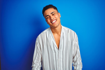 Young brazilian man wearing striped shirt standing over isolated blue background with a happy and cool smile on face. Lucky person.