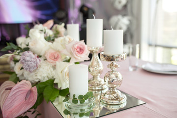 Obraz na płótnie Canvas The wedding table setting for the newlyweds is decorated with fresh flowers of carnation, rose, anthurium and eucalyptus leaves. Silver candlesticks, white candles. Wedding floristry. Closeup details