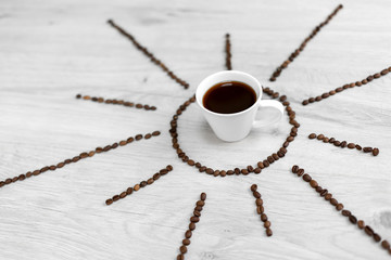 Coffee grains folded in the form of the sun on a wooden background. In the middle is a cup of...