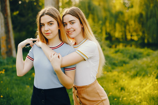 two beautiful young beautiful girls with shiny blond hair and a skirt and walk and spend goood time in a sunny summer park