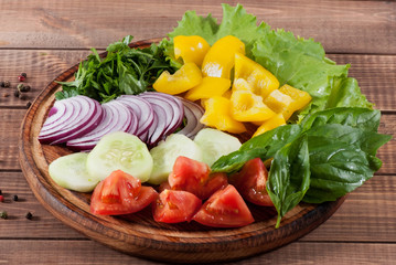 Salad of greens, tomatoes, cucumbers, sweet pepper onions on a wooden background.