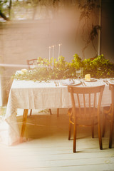 Wedding table with chairs and plates, forks, spoons, knifes on cloth decorated with greenery bouqet
