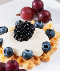 Sweet waffles with sour cream and fruit on a light background.