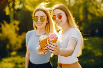 Obraz premium two beautiful young beautiful girls with shiny blond hair and a skirt and walk and spend goood time in a sunny summer park and eating ice cream in a waffle horn