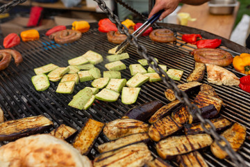 A large round grill on the coals in which grilled color vegetables and fresh meat sausages are cooked. Food and equipment for cooking at a food festival