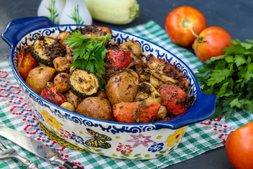 Chicken thighs baked with potatoes, tomatoes and zucchini, located in ceramic form on a dark background, horizontal orientation