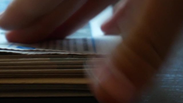 Hands picking up newspapers from pile fast. Close up shot of newspapers piling up. Stack of newspapers on dark background. Side view
