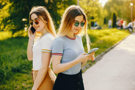 two beautiful young beautiful girls with shiny blond hair and a skirt and walk and spend goood time in a sunny summer park