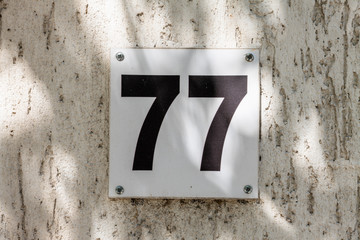 Number 77, seventy-seven, street number sign on the wall	