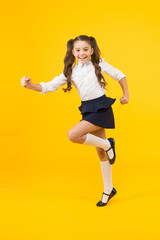Fototapeta na wymiar She is dynamic. Happy energetic schoolchild in motion on yellow background. Little girl with long hair feeling energetic. Small kid getting energetic start to school year. Active and energetic