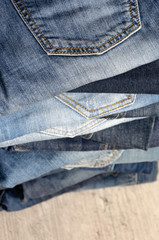 A stack of carelessly folded jeans on wooden background. Close-up of jeans in different colors....