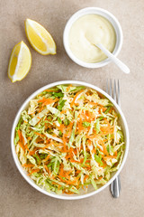 Coleslaw made of freshly shredded white cabbage and grated carrot with homemade mayonnaise-based salad dressing and lemon wedges on the side, photographed overhead (Selective Focus on the salad)