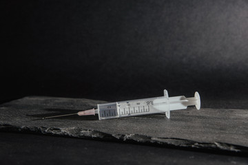 The syringe lies on a stone table top. Medical and pharmaceutical concept. Accepting injections, health problems. Treatment by injection of drugs into a syringe.
