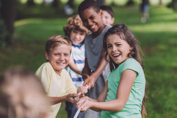 selective focus of cheerful multicultural kids competing in tug of war