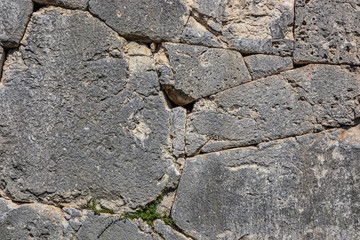 The ancient megalithic walls surround the acropolis of Amelia, in Umbria, Italy. Texture composed ofirregular huge blocks of stone. The grass grows between the interstices of the wall.