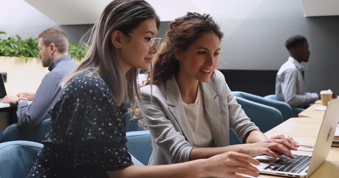 Happy caucasian mentor teaching asian trainee explain computer project