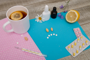 sad face made of pills on a blue background, lemon tea, different pills and medicines for treating colds