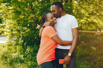 a young and stylish dark-skinned boy in a white T-shirt and his pretty girl in a pink T-shirt standing in a sunny summer park and using the phone