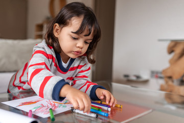 Adorable little girl coloring with crayons at home