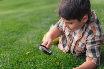 selective focus of boy looking at grass through magnifier