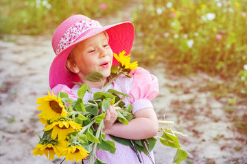 Little girl, a child in a pink dress and a pink hat on the field with flowers. Happiness and joy of childhood. Summer countryside