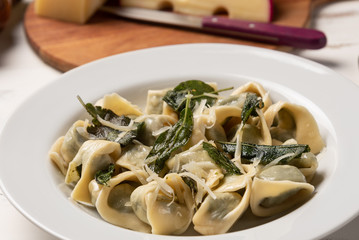 Homemade tortellini with butter and sage in a white plate on white wooden table background. Soft light