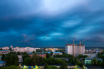 Industrial landscape with silhouettes of cranes on the thunderclouds background