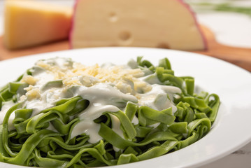 Homemade greeen spinach fettuccine with bechamel sauce in a white plate, rustic wooden table background, soft light. Italian food style