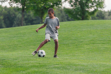cute african american boy playing football on grass