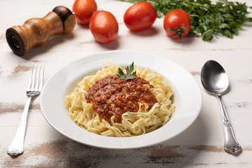 Pasta Fettuccine Bolognese with tomato sauce in a white plate on rustic wooden table background, soft light