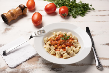 Italian tortellini (capeletti, agnolini) with tomato sauce in a white plate on rustic white wooden table background