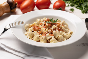Italian tortellini (capeletti, agnolini) with tomato sauce in a white plate on rustic white wooden table background
