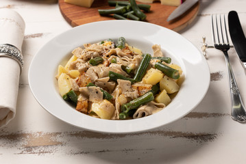 Homemade Pizzoccheri alla valtellinese;  a traditional short tagliatelle pasta typical of northern Italian province of Valtellina. White plate on wooden white  background. Soft light