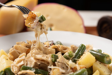 Homemade Pizzoccheri alla valtellinese;  a traditional short tagliatelle pasta typical of northern Italian province of Valtellina. White plate on wooden white  background. Soft light