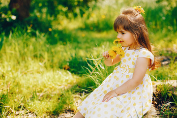 a little girl with beautiful long hair and in a yellow dress is playing in the summer sunshine and sitting on the grass